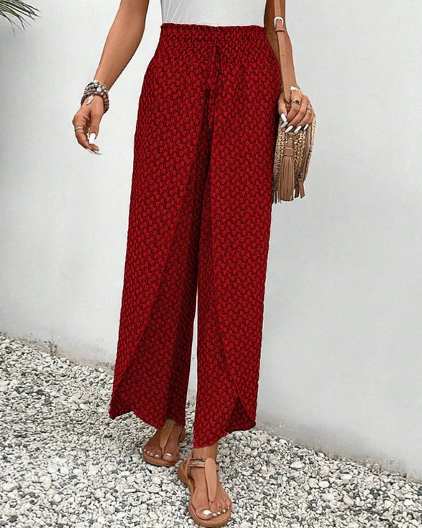 Lucie Women's Smocked Waist Palazzo Trousers in red floral, angled view with tassel bag
