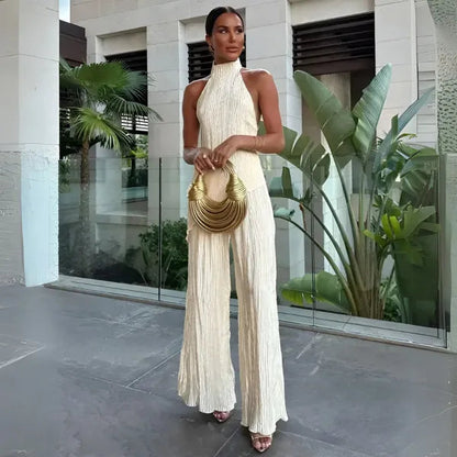 Aira women's halter backless plisse jumpsuit in beige, full front view outdoors