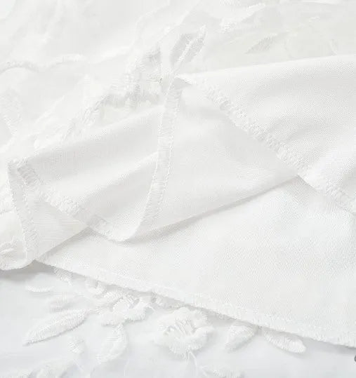 Close-up of the white floral lace fabric and scalloped hem of the Elsie dress