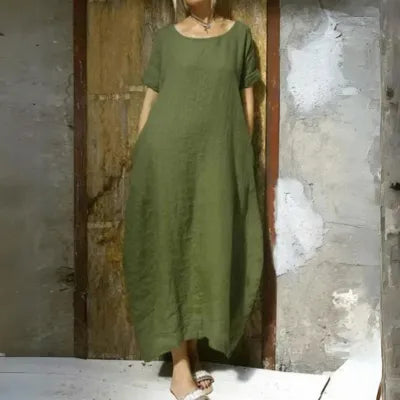 Green Gilda short sleeve caftan maxi dress worn against a rustic wall