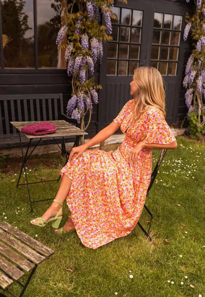 Orange Lotte floral maxi dress shown seated from the side in a garden