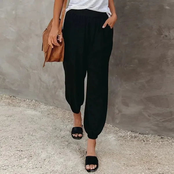 Agnes Women's Smocked Waist Harem Trousers in black, front view with tan bag